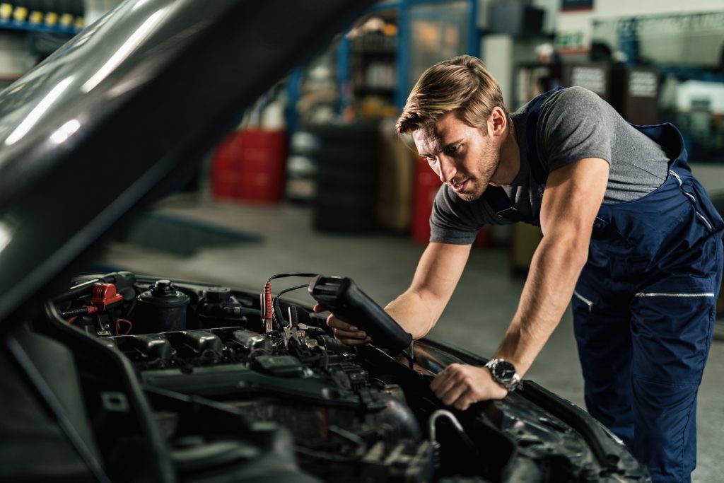 Young mechanic with diagnostic tool analyzing car engine problem